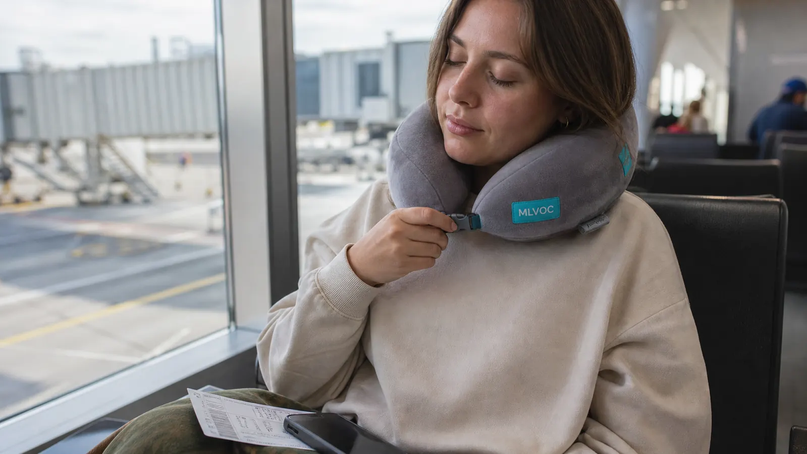Hand adjusting the front clasp of a memory foam neck pillow before boarding at an airport gate
