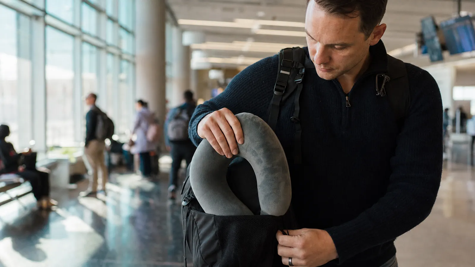 Traveler rolling a neck pillow and stuffing it into the side pocket of a backpack after landing