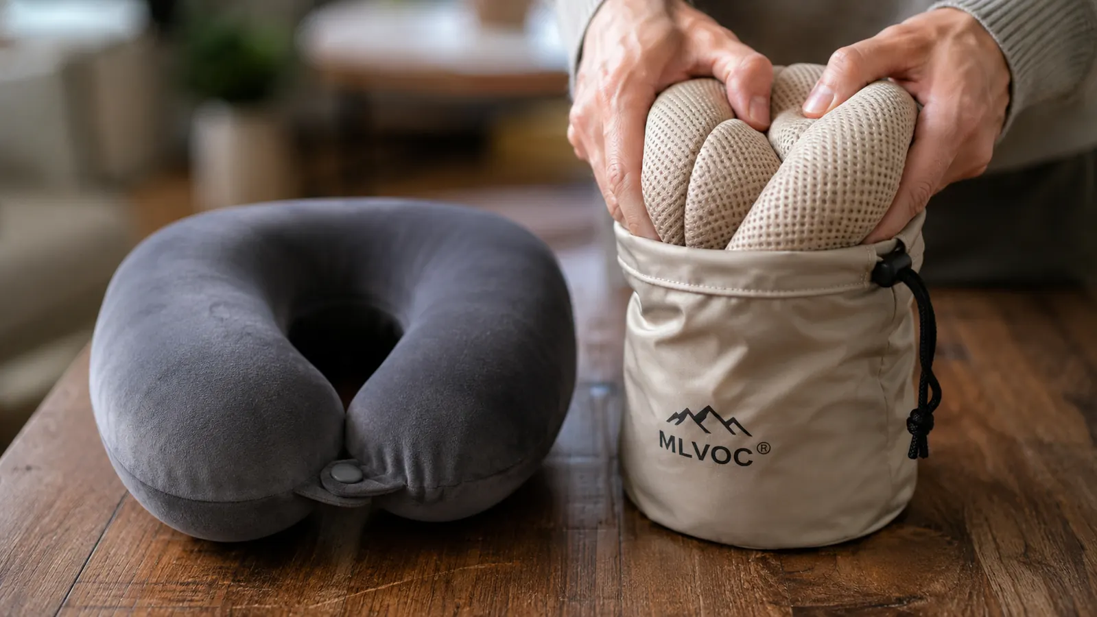 Hand compressing the MLVOC neck pillow into its small drawstring travel bag next to a bulkier folded travel pillow