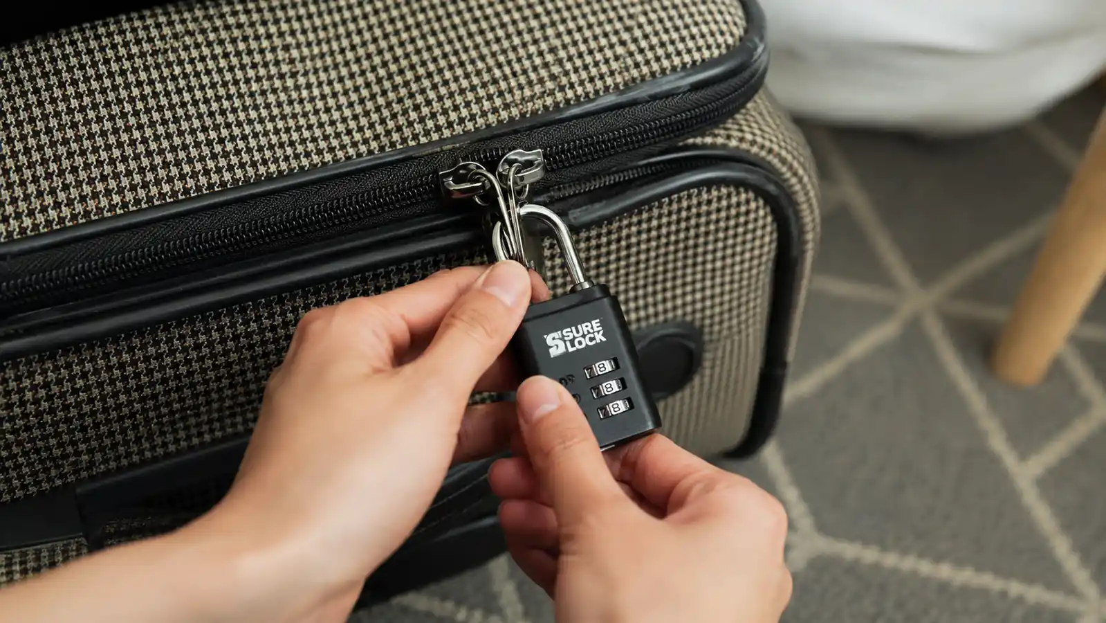Hand clipping a SURE LOCK TSA approved combination lock through the zipper pulls of a packed suitcase
