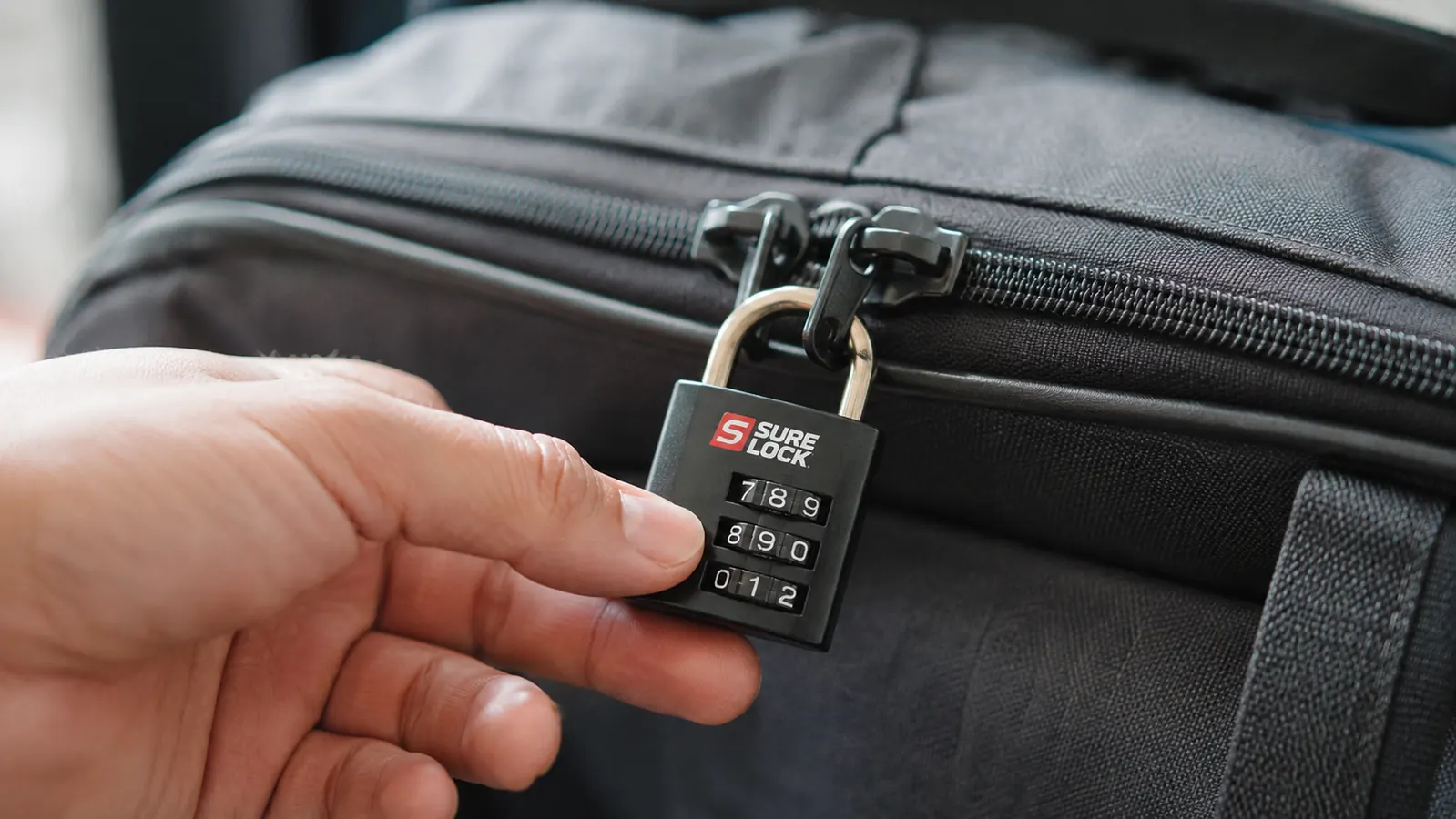 Hand turning the combination dials on a TSA-approved luggage lock clipped to a suitcase zipper
